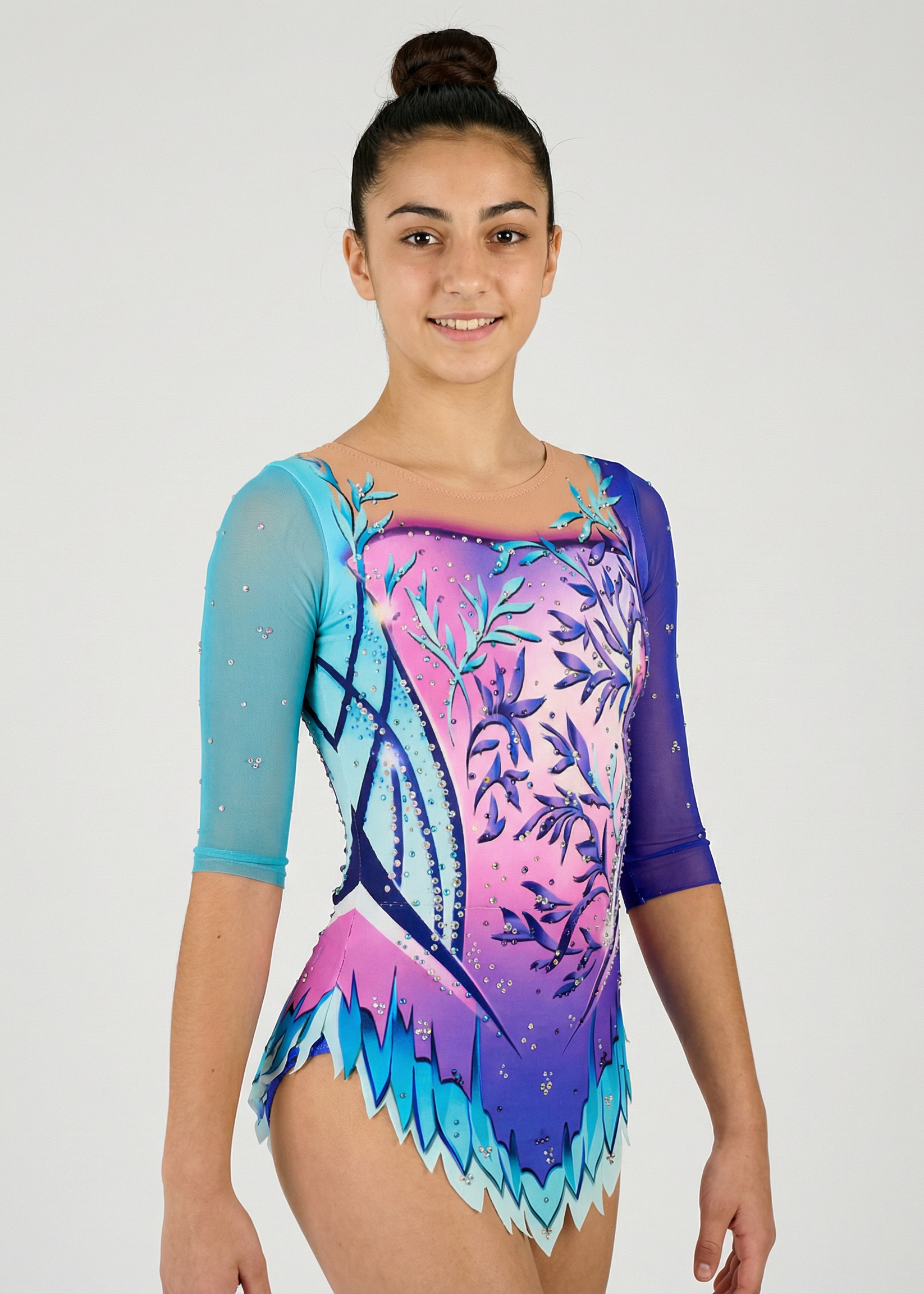Maillot de gimnasia rítmica en degradado rosa-morado con mangas turquesa, pedrería y motivos florales creando un estilo delicado y luminoso.
Maillot rítmico turquesa y morado con degradados, pedrería y detalles florales que aportan un diseño elegante y fantasioso.
Espalda de maillot rítmico en tonos turquesa y morado con transparencias, pedrería y diseño floral con lazos impresos en un estilo mágico.