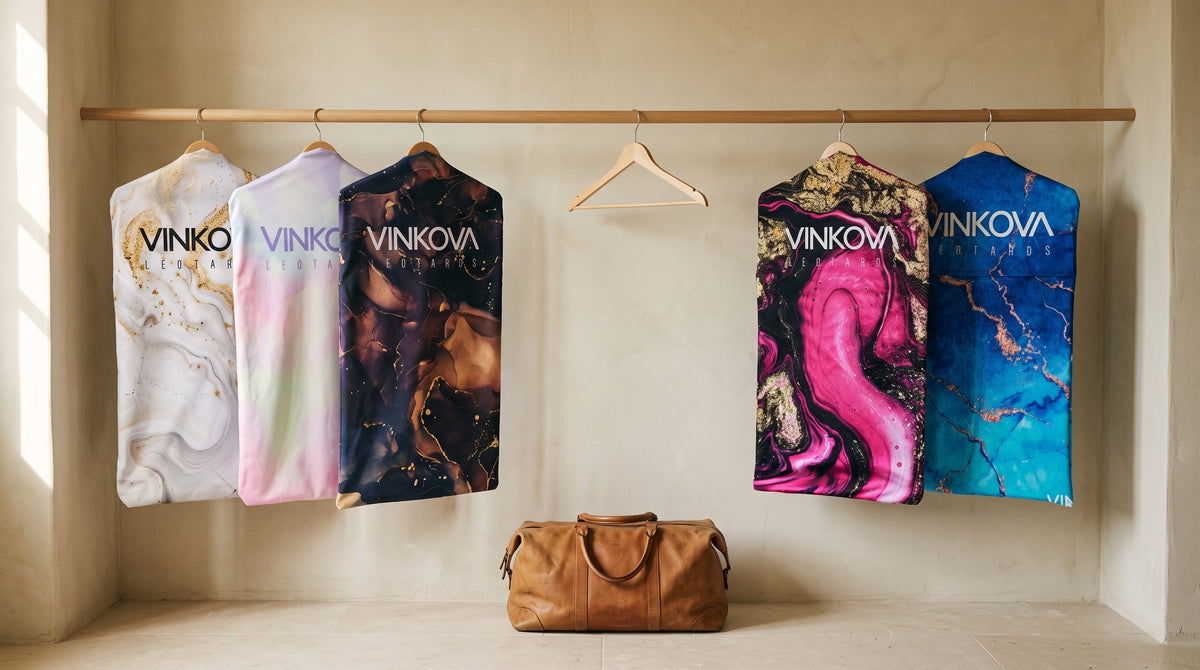 Housses pour justaucorps de gymnastique rythmique VINKOVA à motifs colorés sur des cintres en bois.