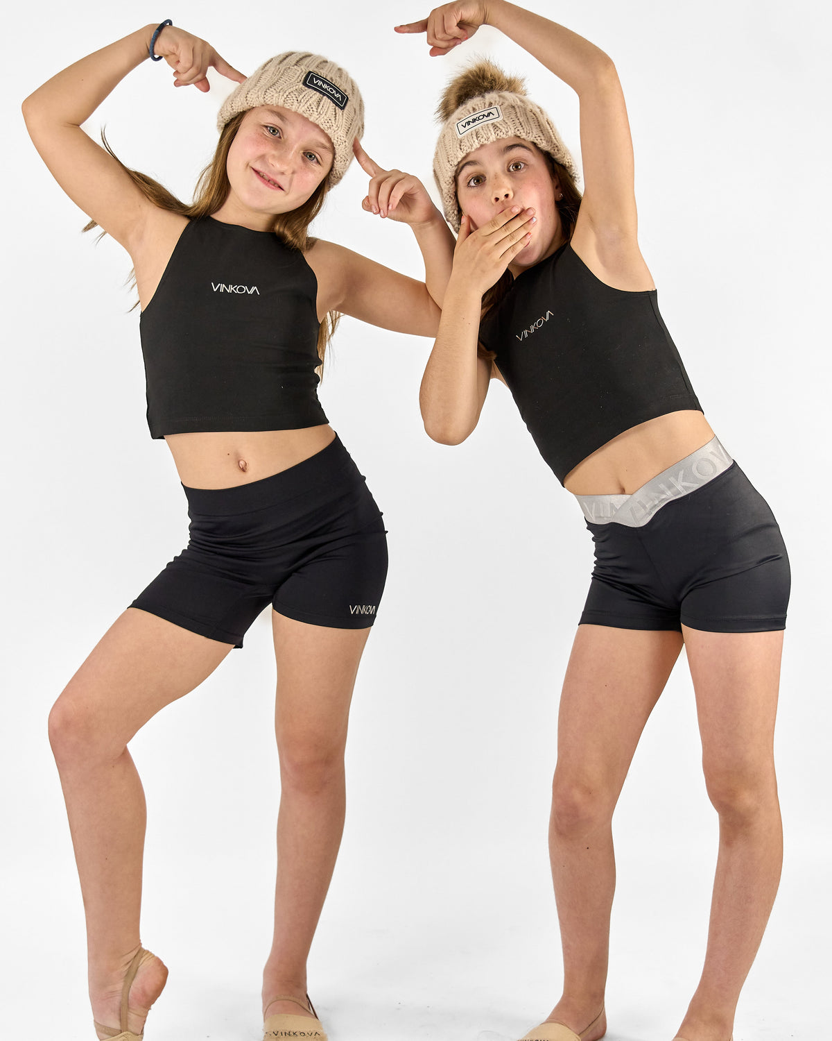 Two gymnasts wearing beige knitted Vinkova winter hats with pompoms.