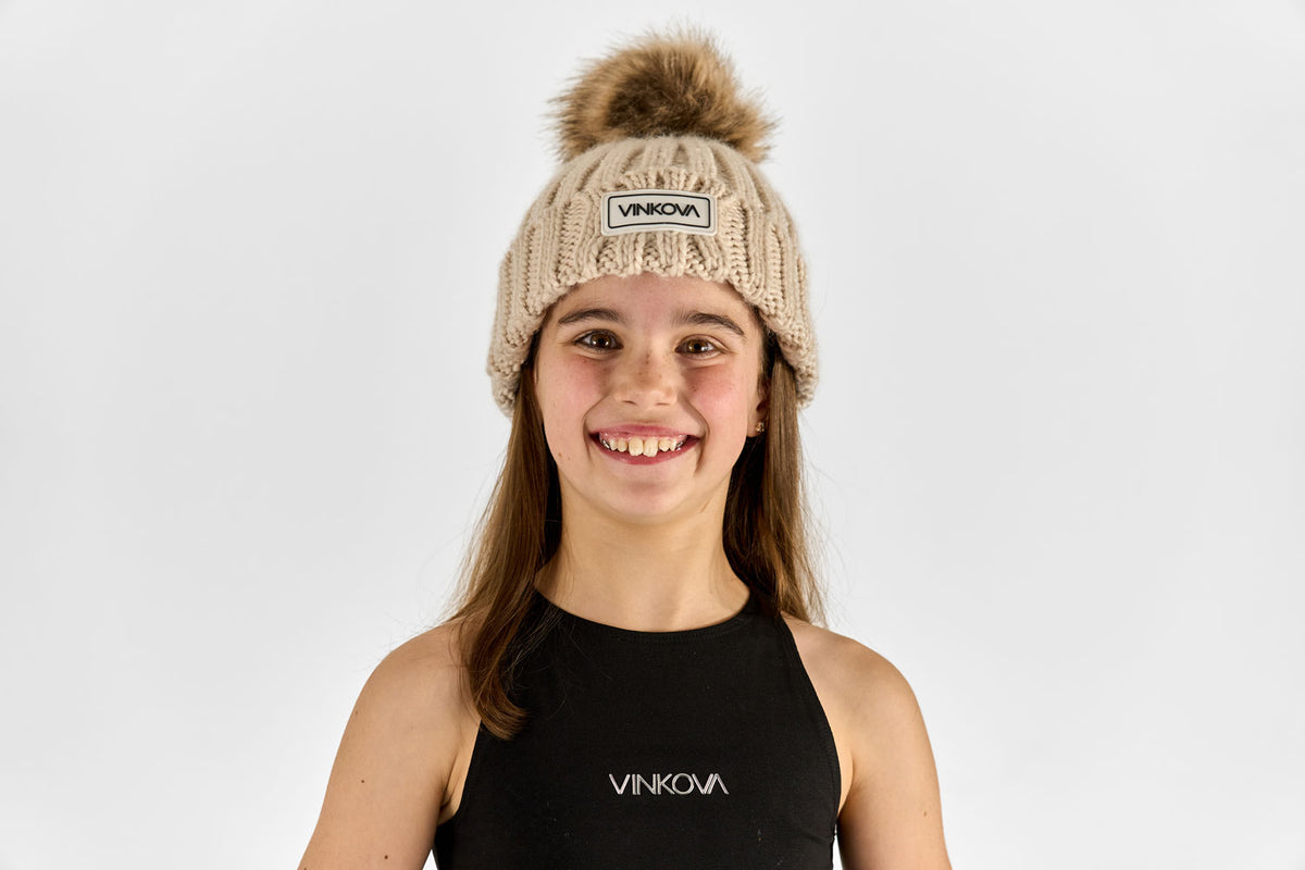 Bonnet d’hiver Vinkova en maille beige à pompon porté par une gymnaste.