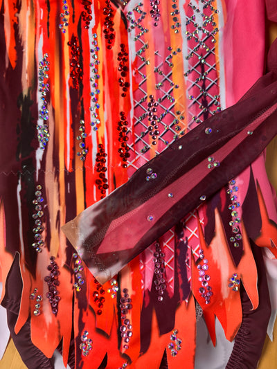 Detalle de la manga larga y el bajo en picos de Goya, con trazos naranjas y magenta y STRASS visible.
